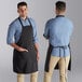 Two men wearing black Choice bib aprons standing on a counter in a professional kitchen.