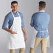 Two men wearing white aprons and blue jeans on a counter in a professional kitchen.