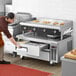 A man in an apron using a Cooking Performance Group countertop electric griddle over a refrigerated base.