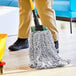 A person holding a Lavex blue and white mop with a yellow handle.