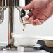 A hand pouring cereal from a Vollrath double canister cereal dispenser into a bowl.