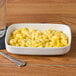 A Tuxton eggshell china bowl filled with macaroni and cheese on a wood table with a fork and spoon.