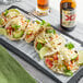 A stone tray with three tacos filled with vegetables and Daiya Vegan Jalapeno Havarti cheese.