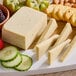 A cutting board with a block of Daiya Vegan Jalapeno Havarti cheese, crackers, and fruit.