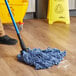 A person mopping a wooden floor with a Lavex Pro blue wet mop.