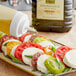 A bottle of Colavita Mediterranean Extra Virgin Olive Oil being poured onto a plate of tomatoes, mozzarella, and basil.