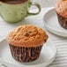 A David's Cookies Healthy Harvest muffin on a white plate next to a cup of coffee.