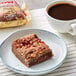 A David's Cookies pecan brownie on a plate next to a cup of coffee.