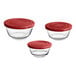 A group of three Anchor Hocking glass mixing bowls with red plastic lids.