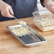 A person in a blue shirt using a spoon to put food in a Vollrath stainless steel hotel pan.