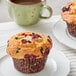 A David's Cookies Mountain Berry muffin on a white plate with a cup of coffee.