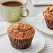 Two David's Cookies Raisin Bran Muffins on a plate next to a cup of coffee.