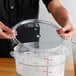 A person holding a Cambro clear round food storage container with a lid filled with white powder.