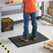 A person wearing blue jeans standing on a black Lavex BubbleFlex anti-fatigue mat.