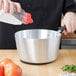 A hand pouring salt into a silver Vollrath sauce pan.