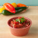 A bowl of salsa on a table with a leafy green garnish.