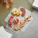 A plate of meat and cheese on a white table with a stack of white plates.