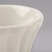 A close up of a Hall China flared ivory ramekin with a curved rim.