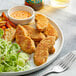 A plate of Rebellyous vegan plant-based chicken tenders with salad and dip, with a fork next to it.