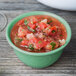 A bowl of GET Diamond Mardi Gras Rainforest Green melamine filled with salsa with a spoon next to it on a wood surface.