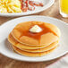 A stack of pancakes with butter on top served on a plate.