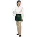 A woman wearing a Chef Revival hunter green waist apron with 3 pockets.