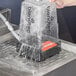 A hand pouring water from a plastic container into a machine.