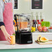 A man in an apron using a Blendtec Stealth 885 blender to make orange juice.