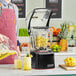 A man pours juice from a plastic container into a Blendtec blender on a counter with a bowl of pineapple chunks nearby.