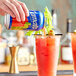 A hand pouring Clamato Original Tomato Cocktail from a can into a glass of red liquid.