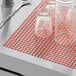 Red plastic mesh shelf liner on a counter with glasses.