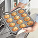 A person holding a Choice muffin and cupcake pan filled with muffins.