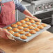 A woman holding a Choice muffin pan filled with muffins on a wooden counter.