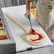A man using a Choice wooden pizza peel to spread sauce on a pizza.