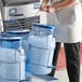 A woman wearing an apron holds a blue Vigor ice tote filled with ice.