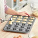 A woman using a Choice mini muffin pan to put food in.