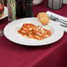 A Tuxton bright white china bowl filled with lasagna and bread on a table.