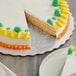 A cake with green and yellow frosting on a silver Enjay cake circle with a slice cut out.