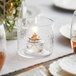 An Acopa glass candle holder with a lit candle on a table in a fine dining restaurant.