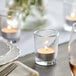 A table setting with a candle in a clear glass votive holder.