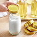 A person's hand holding a gold lid over a glass jar.