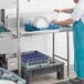 A man in a blue apron washing dishes on a Regency right clean dish table.