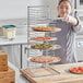 A woman's hand places a pizza on a Choice pizza pan rack.