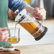 A person using an Acopa French coffee press to pour coffee into a glass cup.