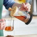 A person using an Acopa glass French coffee press to pour a drink.