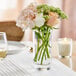 An Acopa cylindrical glass vase with flowers and candles on a table.