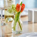 An Acopa urn glass bud vase with flowers on a table.