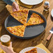 A round, hard coat anodized aluminum pizza pan with a tapered edge, holding several slices of pizza.