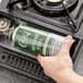 A hand holding a green Choice Butane Fuel canister over a lit stove.