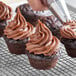 A person's hand using a pastry bag to frost a chocolate cupcake.